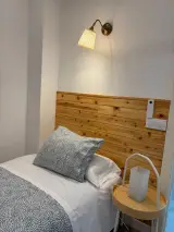 Cama individual con almohadas estampadas, lámpara de pared y mesita con lámpara de mesa